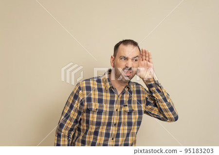 Listening man holds his hand near his ear on a beige background. Handsome man trying to listen to someone's conversation 95183203