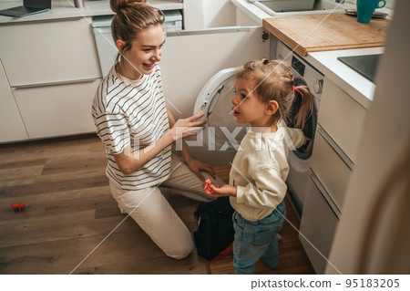 Female and her child putting dirty clothes into the washer Female and her child putting dirty clothes into the washer 95183205
