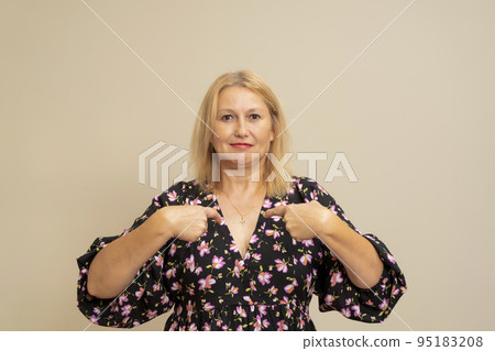 Portrait of a charming happy woman in a dark dress smiling and pointing at herself, proud of her own success, bragging about her achievements. Indoor studio shot isolated on beige background Portrait of a charming happy woman in a dark dress smiling and pointing at herself, proud of her own success, bragging about her achievements. Indoor studio shot isolated on beige background 95183208