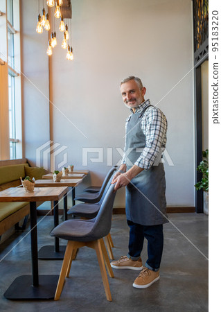 Waiter putting chairs in order in the cafe premises Waiter putting chairs in order in the cafe premises 95183220