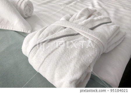 There are clean white towels and a bathrobe on the bed. 95184021