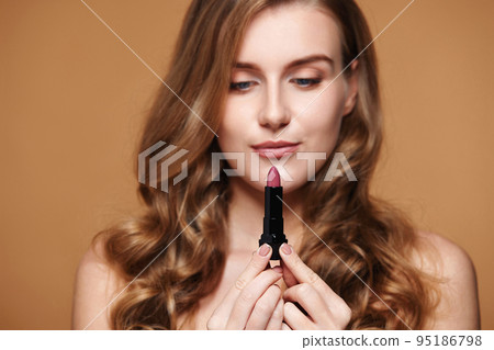 beautiful woman holding nude lipstick on beige background beautiful woman holding nude lipstick on beige background 95186798