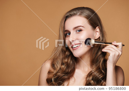 smiling woman applying blush on cheeks with make-up brush 95186800
