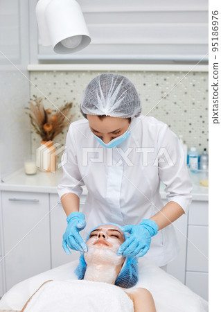 beautician applies the mask to the face of beautiful woman 95186976