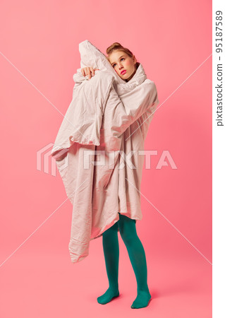 Beautiful young girl wrapped in soft blanket standing isolated over pink background. Comfrort, fashion, art, creativity Beautiful young girl wrapped in soft blanket standing isolated over pink background. Comfrort, fashion, art, creativity 95187589