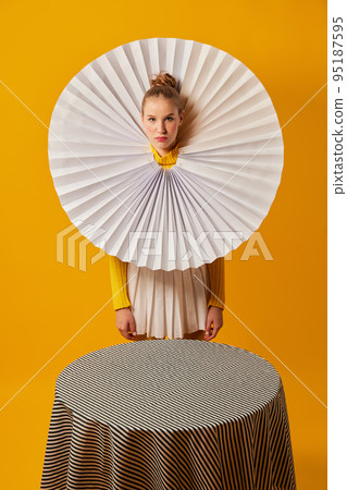 Lamp. Young indifferent girl in giant jabot collar or neckwear and yellow tights isolated over yellow background. Contemporary art, weird beauty, fashion 95187595