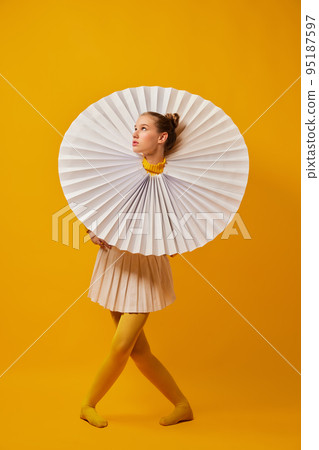 Dance. Young indifferent girl in giant jabot collar or neckwear and yellow tights isolated over yellow background. Contemporary art, weird beauty, fashion 95187597
