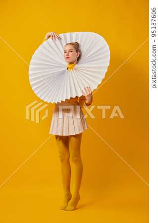 Young indifferent girl in giant jabot collar or neckwear and yellow tights isolated over yellow background. Contemporary art, weird beauty, fashion Young indifferent girl in giant jabot collar or neckwear and yellow tights isolated over yellow background. Contemporary art, weird beauty, fashion 95187606