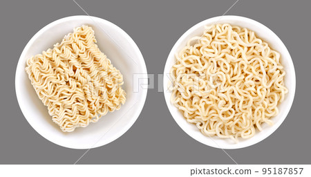 Instant ramen, in white bowls. Dried block of instant noodles, and the same amount of noodles, soaked in boiling water. Isolated, on gray background, macro food photo. 95187857