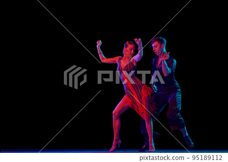 Stylish ballroom dancers couple in gorgeous outfits dancing in sensual pose on dark background in neon light. Concept of art, music, dance, emotions. Stylish ballroom dancers couple in gorgeous outfits dancing in sensual pose on dark background in neon light. Concept of art, music, dance, emotions. 95189112