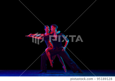Stylish ballroom dancers couple in gorgeous outfits dancing in sensual pose on dark background in neon light. Concept of art, music, dance, emotions. Stylish ballroom dancers couple in gorgeous outfits dancing in sensual pose on dark background in neon light. Concept of art, music, dance, emotions. 95189128