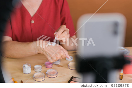 Closeup beauty blogger or influencer with makeup product recording video in room at home. Using ring lamp and smartphone 95189878