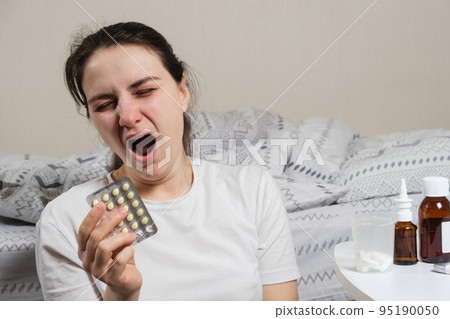 A woman with insomnia sits by the bed and holds pills for healthy sleep and yawns. 95190050