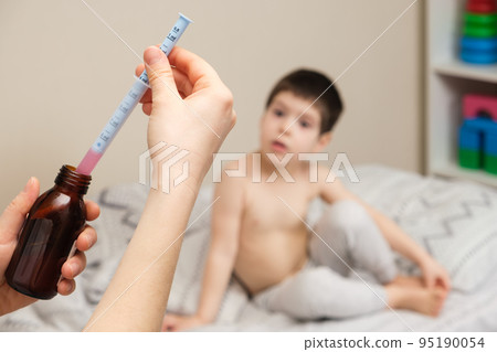 The pediatrician or mother types in a measuring syringe the medicine for cough or temperature syrup for the child The pediatrician or mother types in a measuring syringe the medicine for cough or temperature syrup for the child 95190054