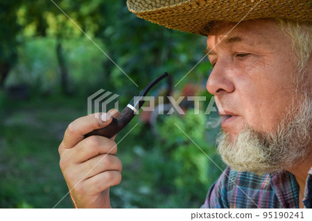 Senior adult man with white beard smoking tobacco pipe outdoors Senior adult man with white beard smoking tobacco pipe outdoors 95190241
