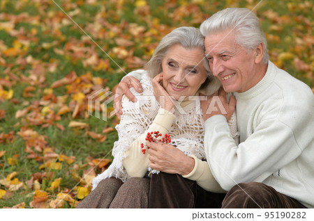 Elderly couple sitting together in the park on the grass in autumn 95190282