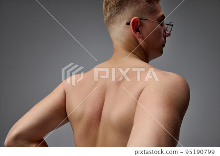 Portrait of young muscular man posing shirtless isolated over grey studio background. Pains in back, spine. Medical massage treatment 95190799