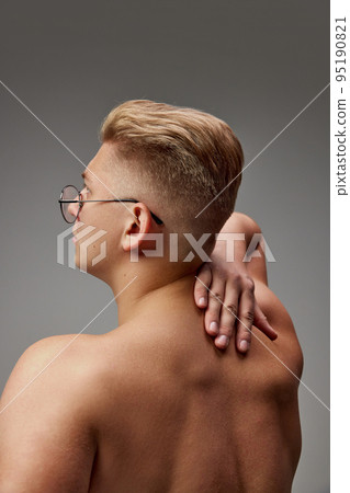 Portrait of young muscular man posing shirtless isolated over grey studio background. Medical massage of back Portrait of young muscular man posing shirtless isolated over grey studio background. Medical massage of back 95190821