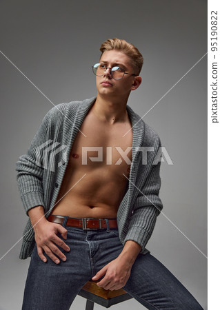 Portrait of stylish young man with muscular body posing in knitted sweaterm jeans and glasses isolated over grey studio background 95190822