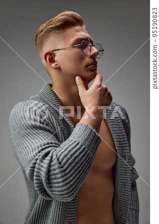 Portrait of brutal young man with muscular body posing in knitted sweater and glasses isolated over grey studio background 95190823