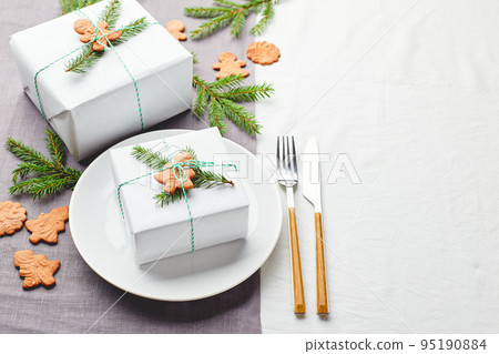 Christmas festive table setting, plate with gift decorated with spruce sprigs and gingerbread Christmas festive table setting, plate with gift decorated with spruce sprigs and gingerbread 95190884