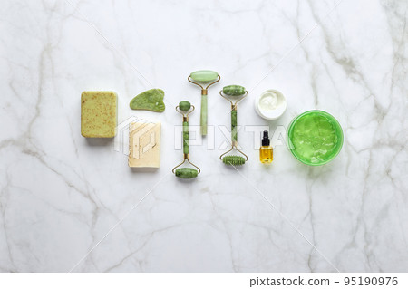 Cosmetic skin care products, jade stone face massager, creams, gel and oil. Roller massage of the face. Flat lay, top view 95190976