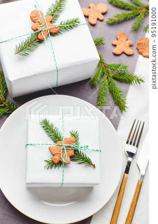 Christmas festive table setting, plate with gift decorated with spruce sprigs and gingerbread Christmas festive table setting, plate with gift decorated with spruce sprigs and gingerbread 95191000