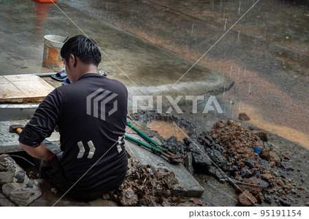 Utility worker using tool to fixing broken water main for commercial building water supplies during a rain. Utility worker using tool to fixing broken water main for commercial building water supplies during a rain. 95191154