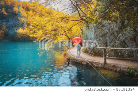Woman with red umbrella on path under yellow trees near lake Woman with red umbrella on path under yellow trees near lake 95191354