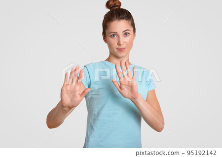 Stop it! Pretty young woman with appealing look, keeps palms over chest, makes refusal gesture, dressed in casual t shirt, isolated over white background. People, youth and body language concept 95192142