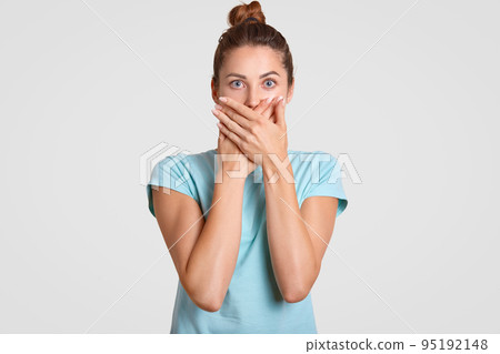 Keep silence, please. Frightened woman covers mouth with both palms, looks with scared expression directly at camera, wears casual t shirt, keeps information in secret. Speak no evil concept. Keep silence, please. Frightened woman covers mouth with both palms, looks with scared expression directly at camera, wears casual t shirt, keeps information in secret. Speak no evil concept. 95192148