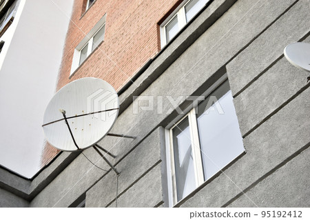Satellite dish on a gray building close-up. A parabolic antenna on the wall. 95192412