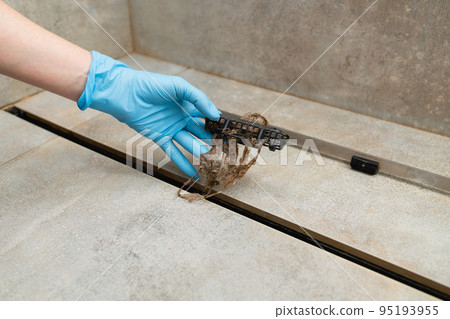 Woman removing hair clump from the shower drain. 95193955