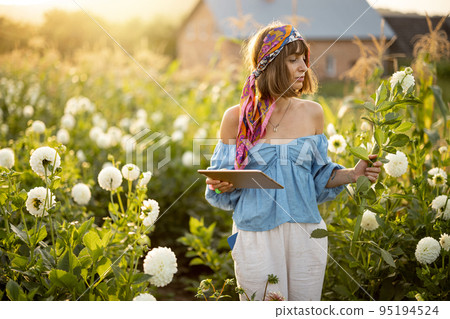 Woman with a digital tablet on flower farm outdoors Woman with a digital tablet on flower farm outdoors 95194524