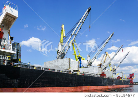 Large bulk cargo ship with open holds in the port cargo terminal, blue sky background 95194677