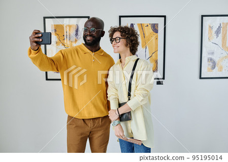 Young multiethnic couple taking selfie on smartphone while visiting art gallery 95195014