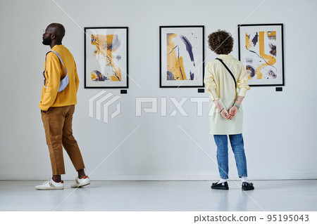 Rear view of young people looking at paintings on the wall at art gallery 95195043