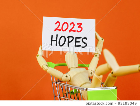 2023 Hopes symbol. White paper with words 2023 Hopes, human model in shopcart. Beautiful orange table orange background. Business and 2023 hopes concept. Copy space. 95195049