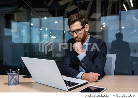 Serious thinking businessman working inside office building, man pondering important decision, boss in business suit using laptop at work. 95195169
