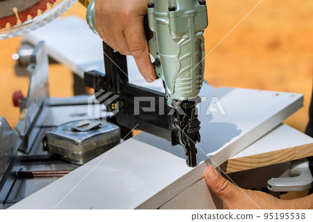 Assembling wood boards with nails with pneumatic air gun is done by carpenter 95195538