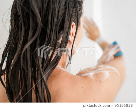 Naked woman with takes a shower. Woman washes her arms with shower gel and blue washcloth. Morning routine in urban apartment. 95195838