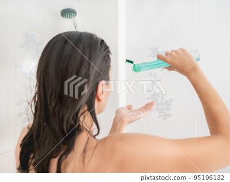Naked woman with short hair takes a shower. Woman squeezes shampoo out of plastic bottle. Usual routine in white bathroom. 95196182