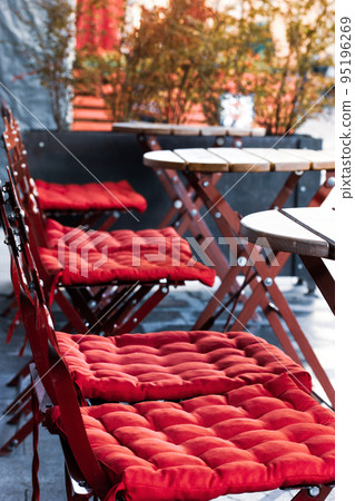 Classic empty cafe restaurant terrace after rain without people. Folding chairs with red soft cushions, wooden round tables on cafeteria patio Garden furniture. Nice area for relaxing on a city street 95196269