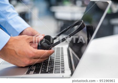 A man puts a headset on a laptop keyboard in the office. 95196961