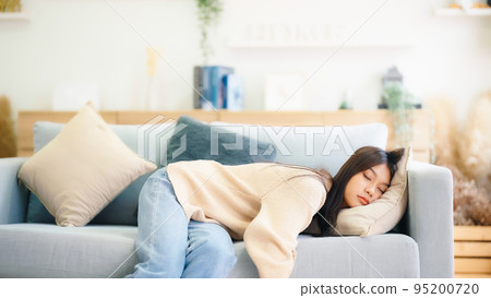 Asian woman resting at home on couch, feeling exhausted after work 95200720