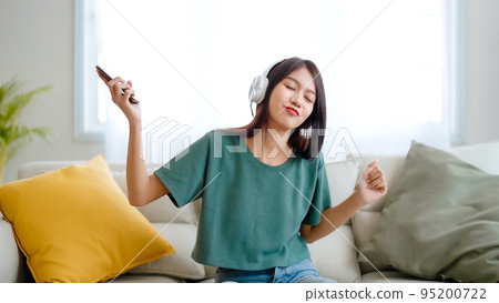 Young asian woman listening to music on couch in living room at home 95200722