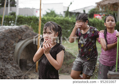 Group of happy children girl playing in wet mud puddle during raining in rainy season Group of happy children girl playing in wet mud puddle during raining in rainy season 95201007