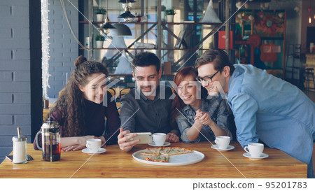 Young people are having funny video chat holding smartphone looking at webcam chatting to friend at table inside nice cafe. Modern communication and friendship concept. 95201783