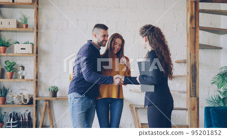 Friendly realtor is giving keys to young couple buyers of new house, happy spouses are hugging , smiling man is shaking hands with broker making deal. Friendly realtor is giving keys to young couple buyers of new house, happy spouses are hugging , smiling man is shaking hands with broker making deal. 95201852
