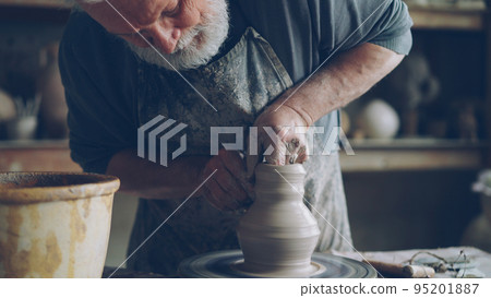 professional male potter creating jar from brown clay in workplace using throwing-wheel. Traditional pottery, handmade utensils and hardworking people concept. 95201887